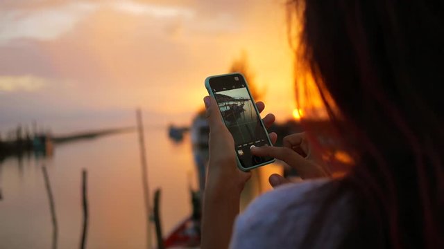 Caucasian Girl Taking Photo of Beautiful Sunset Using Mobile Phone at Fishermans Pier. HD Slowmotion. Thailand.