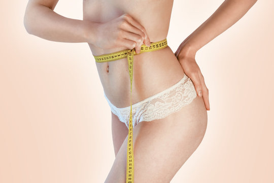 Woman measuring her waistline. Perfect Slim Body. Diet. Young girl measuring waist with a beige background