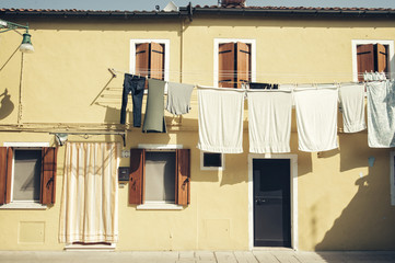 Beautiful house facade on Burano island, north Italy. Yellow house wall with a door, windows and laundry, drying outdoor