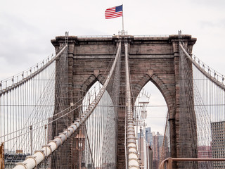 Obraz premium American flag waving on top of Brooklyn Bridge tower, New York City, NY, USA