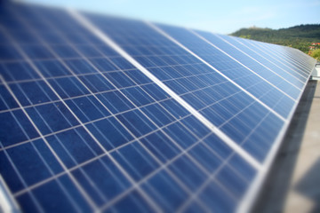 Lots of solar panels are there on a roof of a house. The sun is shining and it is a warm summer day.