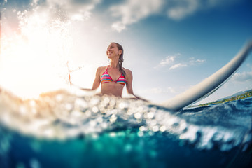 Happy smiling woman sits on the surfboard in the ocean. Tilt shift effect, image has blurred edges.