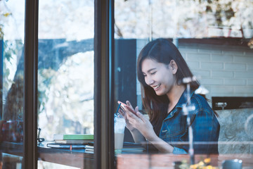 Asia teenage sitting alone using cellphone with smiling in cafe.