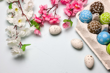 Fototapeta na wymiar Painted easter eggs and branches of spring sakura closeup on a light blue background with space for congratulation