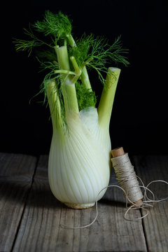Fennel Bulb. Single fresh fennel bulb with leaves on wooden table, black background. Close up organic vegetables.