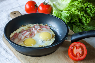 Scrambled eggs and bacon on frying pan on table close-up