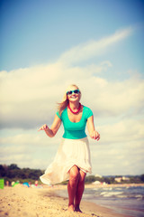 Blonde woman wearing dress playing jumping on beach