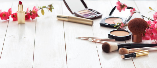 Various cosmetic products for make-up with pink flowers on a white wooden background with copy...