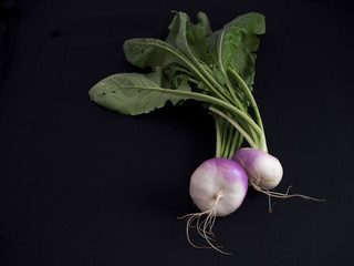 Fresh white and purple turnips with green leaves isolated on black background
