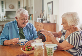 Smiling senior woman pouring her husband a coffee over breakfast - Powered by Adobe