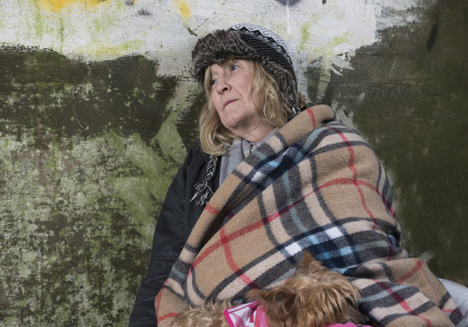 Mature homeless woman leaning against an old wall 