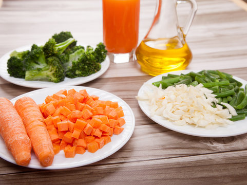 Carrots, broccoli, beans, cabbage, carrot juice and vegetable oil on a wooden background