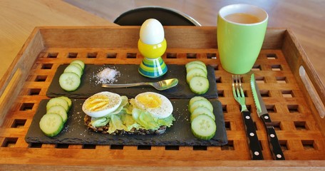 Wooden tray with healthy meal containing of rye bread, boiled eggs, lettuce and cucumber