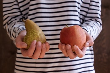 Junge Frau hält eine Birne und einen Apfel in den Händen
