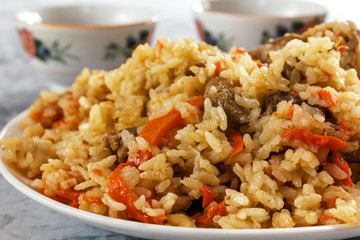Friable pilaf with meat on a background of cups with tea. Closeup
