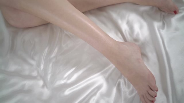 Top view of young woman sleeping in bed perfect female legs on white silk linen
