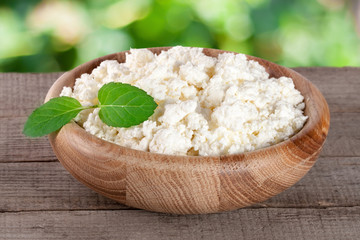 Cottage cheese in a wooden bowl on board with blurred garden background