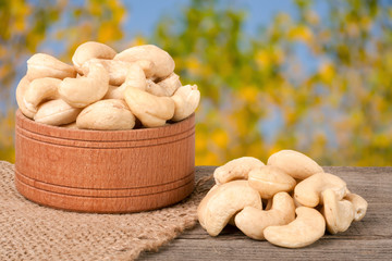 cashew nuts in a wooden bowl on the board with blurred garden background