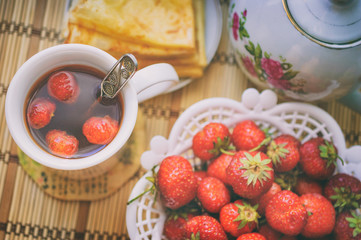 Crepes and Fresh strawberry tea in white cup, teapot, ripe strawberries in a vase and crepes. Breakfast composition for country family in the morning, top view. Image with filter effect instagram