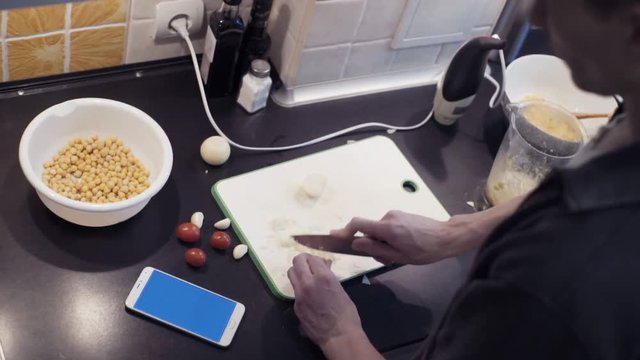Hands of young man cutting garlic at home kitchen preparing vegetable