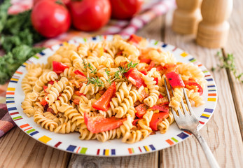 Fusilli Italian whole wheat pasta in tomato vegetarian sauce with sweet red peppers decorated with thyme on a wooden table.
