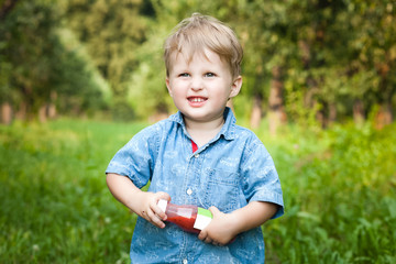 Little boy walks alone in a meadow and drinks juice