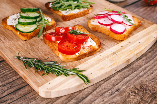 Four sandwiches with fresh vegetables, tomatoes, cucumbers, radish and arugula on a wooden background. Homemade butter and toast. selective focus.