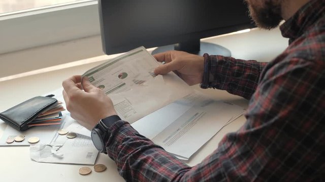 Man opens envelope with hosehold bill, takes out paper with wasting diagram scheme and letter witn total sum to pay, reads it horoughly and desperately wides his hands