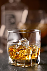 Whiskey glass close-up. Cold with ice, bottle in the background