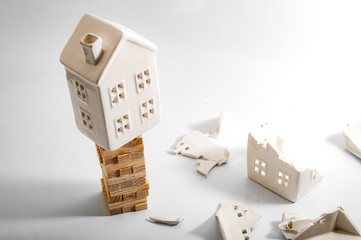 Financial risk, unstable real estate investment and shaky housing market concept with a home on stacked wooden building blocks surrounded by the ruins and debris of another house that collapsed