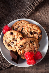 Chocolate chip cookies on white plate dark old wooden table with red raspberry and  place for text.,  freshly baked. Selective Focus with Copy space..
