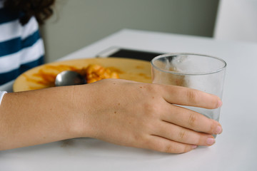 young girl drinking water and eating  at home with smartphone on the table