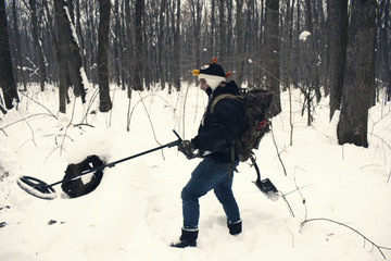 Young man metal detecting in snow holding metal detector 