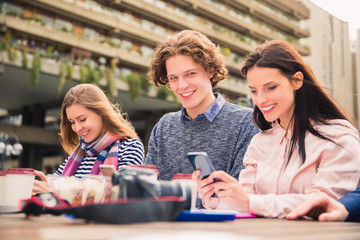 Fototapeta premium Interesting smiling students sit with their phones in time of a break, outdoors