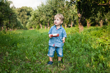 Little boy walks alone in a meadow and drinks juice