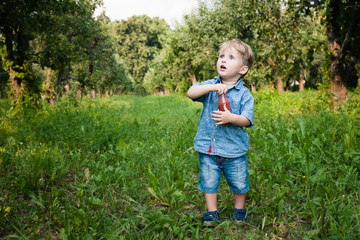 Little boy walks alone in a meadow and drinks juice