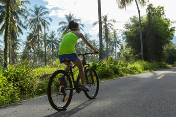 Obraz premium Young woman cycling on tropical forest trail