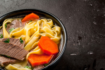 Beef soup with noodles and carrots in the Asian style. With chopsticks, on the black concrete table, copy space