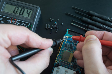 pov shot of technician hands measure voltage, amperage on broken smartphone by multimeter with...