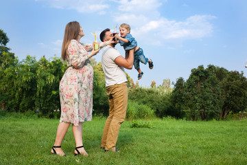 Fototapeta premium Young attractive family playing with child in a meadow and drinking juice