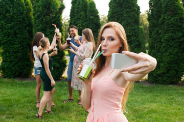 Friends rest and drink juice in the garden, and the girl makes selfie