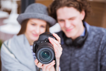 In the front plan is photo camera, on background are beautiful couple who looks at photo camera, outdoors