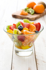 Fruit salad in crystal bowl on white wooden table.
