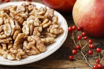 Bowl of walnuts and red apples on wooden table