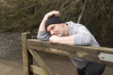 Casual mature man leaning against an old wooden gate outdoors 