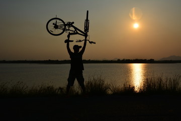 people lift the bicycle up on nature background with sun, silhouette style