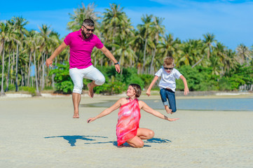Family of three running and jumping along the tropical beach, laughing and enjoing time together
