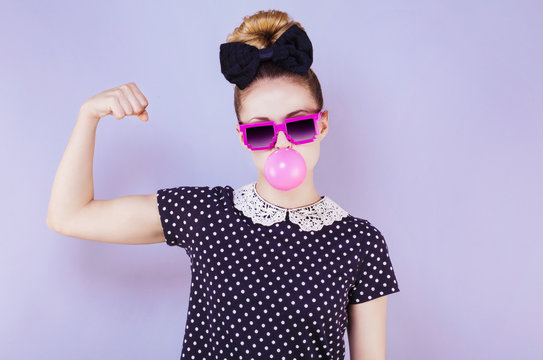 Portrait humoristique d'une jeune femme faisant une bulle de chewing gum en montrant son biceps 