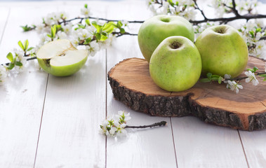 Ripe green apples with spring flowers on a white wooden background.
