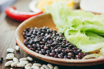 Black beans on brown pottery plate over wooden board.